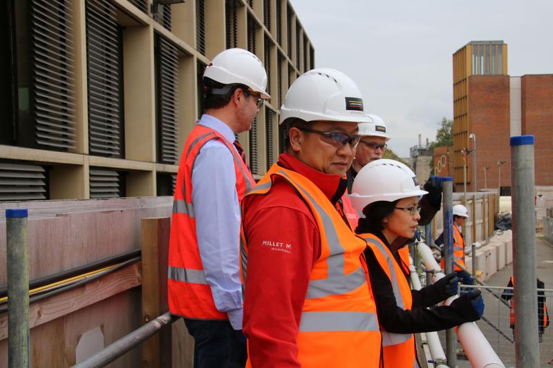 Safety visitors from Hong Kong Andy Fong and Dr May Chan stood wearing high-visibility jackets and hardhats at the Stephen A Schwarzman Centre for the Humanities building site